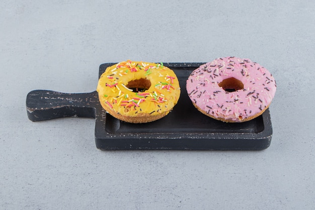 Donuts amarelos e rosa decorados com granulado na tábua. foto de alta qualidade