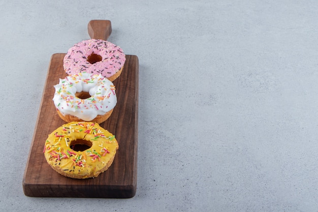 Donuts coloridos decorados com granulado na placa de madeira. foto de alta qualidade