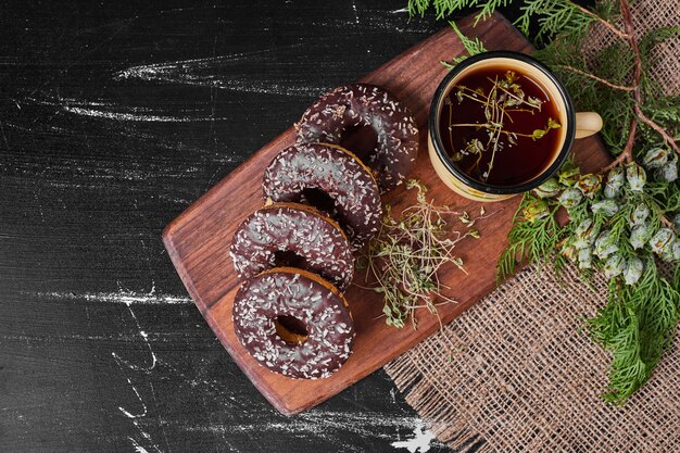 Donuts de chocolate em uma travessa de madeira com chá.