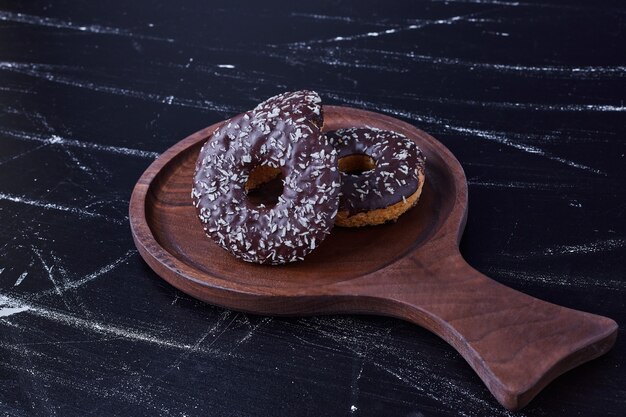 Donuts de chocolate isolados na superfície preta em uma bandeja de madeira.