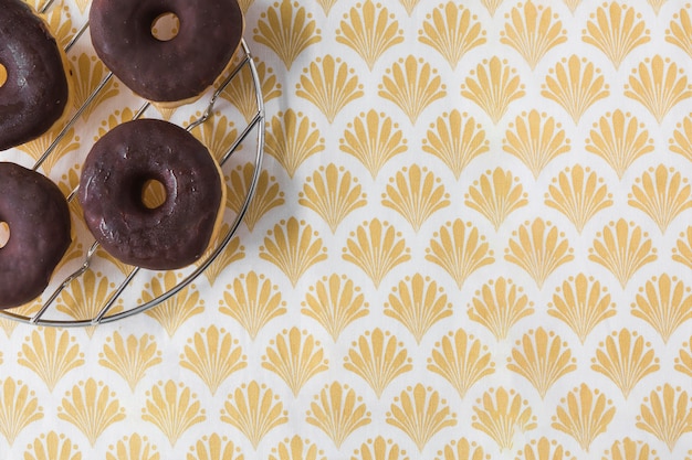 Foto grátis donuts de chocolates em rack de metal sobre o papel de parede dourado