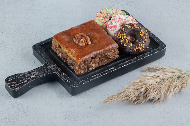 Foto grátis donuts e um bakhlava em uma pequena bandeja ao lado de um talo de grama de penas no fundo de mármore.
