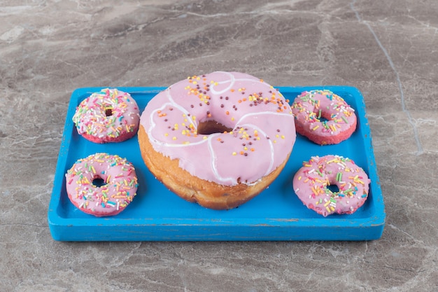 Donuts grandes e pequenos dispostos em uma bandeja azul na superfície de mármore