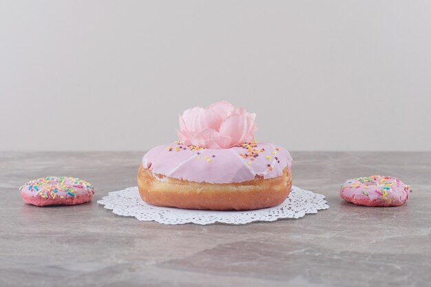 Donuts pequenos ao lado de um donut grande adornado com uma flor no mármore