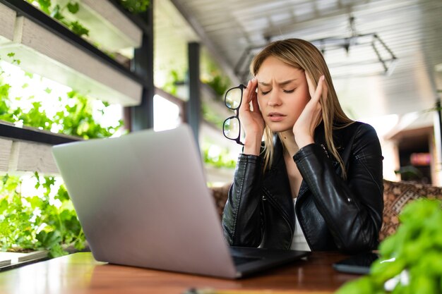 Dor de cabeça de mulher freelance cansada, stess ou prazo com laptop digital trabalhando no local de trabalho em cafeteria.