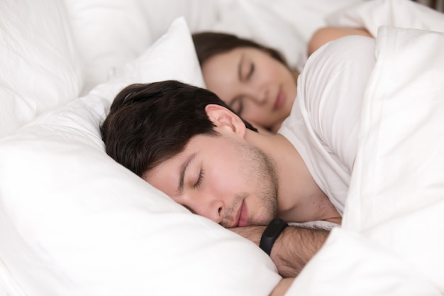 Dormir jovem casal na cama, homem vestindo rastreador relógio inteligente