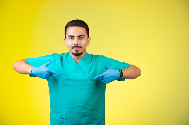 Doutor de uniforme e máscara de mão apontando a si mesmo.