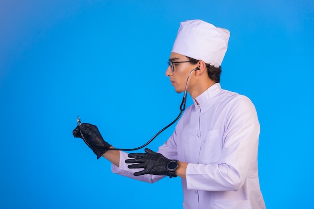 Doutor em uniforme médico branco, verificando com estetoscópio no azul.