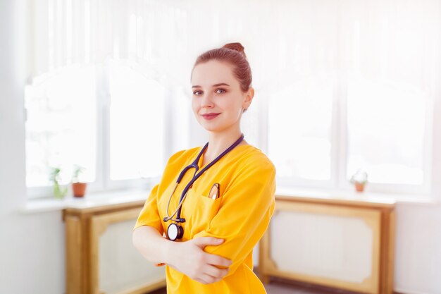 Doutor linda garota sorrindo. retrato em uniforme amarelo com um estetoscópio para o corredor do hospital. cuidados de saúde. fundo.