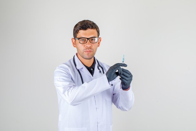 Doutor, segurando a seringa enquanto olha para a câmera no jaleco branco com estetoscópio