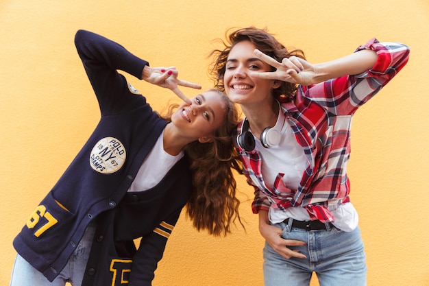 Foto grátis duas adolescentes felizes mostrando o gesto de paz enquanto se diverte