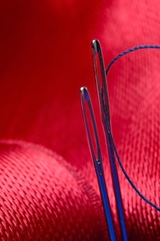 Duas agulhas de costura com linha azul sobre um fundo de tecido vermelho. fechar-se. Foto Premium