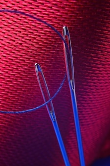 Duas agulhas de costura com linha azul sobre um fundo de tecido vermelho. fechar-se.