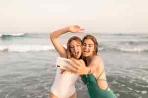 Foto grátis duas amigas alegres tomando selfie na frente de ondas do mar