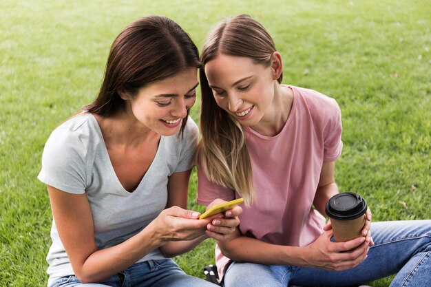 Duas amigas ao ar livre com smartphone e café
