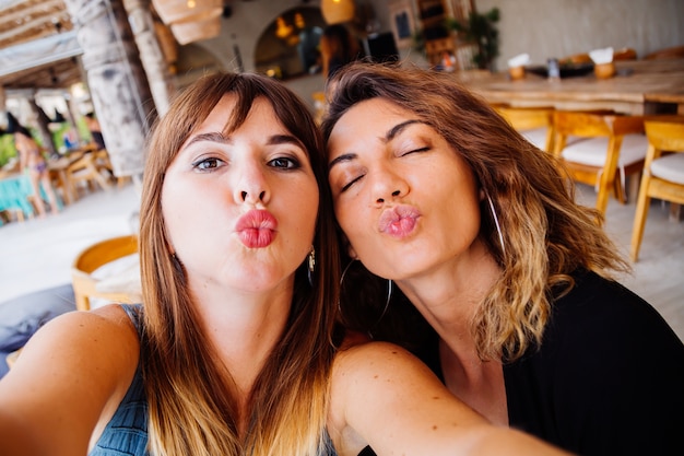 Duas amigas brancas europeias com maquiagem natural e cabelo curto tirando selfie no café de verão