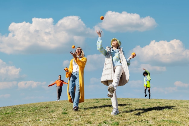 Duas amigas brincando com laranjas e outras duas dançando em um campo ao ar livre