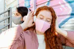 Foto grátis duas amigas com máscaras ao ar livre ouvindo música em fones de ouvido