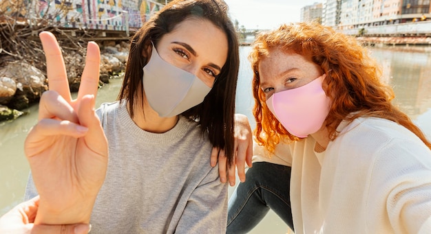 Duas amigas com máscaras ao ar livre tirando uma selfie juntas