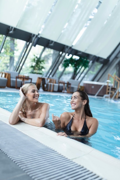 Duas amigas em trajes de banho sentados à beira da piscina aproveitando as férias de verão na piscina interna