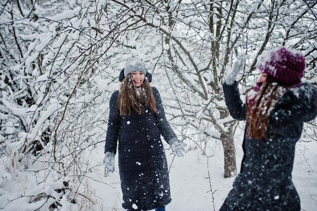 Duas amigas engraçadas se divertindo no dia de neve de inverno perto de árvores cobertas de neve