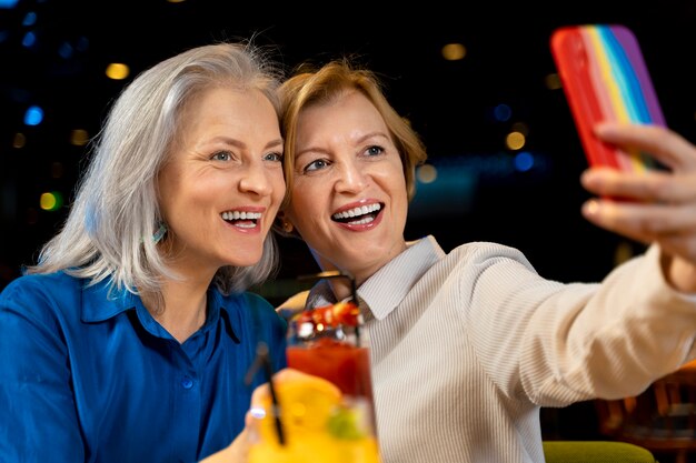 Duas amigas mais velhas tirando uma selfie com suas bebidas em um restaurante