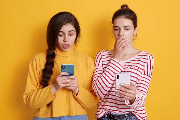 Duas amigas segurar telefones nas mãos e olhando para telas com grandes olhos