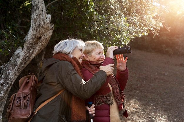 Duas amigas seniores desfrutando de uma caminhada na natureza enquanto usam binóculos