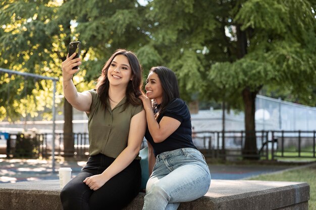 Duas amigas tirando uma selfie no parque enquanto tomam um café