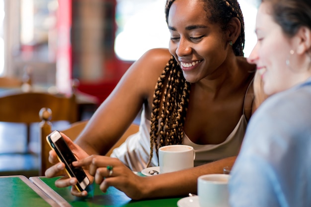 Duas amigas usando um telefone celular enquanto bebia uma xícara de café em uma cafeteria. conceito de amigos.