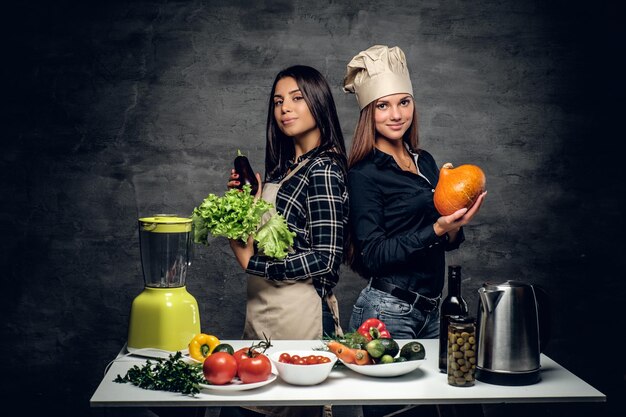 Duas atraentes chefs começam a preparar suco de vegetais no liquidificador.