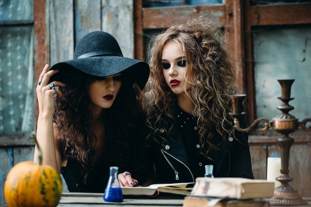 Duas bruxas vintage sentadas à mesa em um lugar abandonado na véspera do halloween Foto gratuita