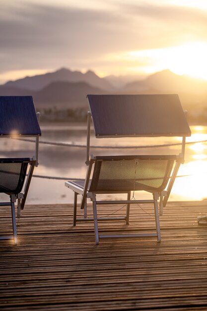 Duas cadeiras vazias em um píer de madeira ao pôr do sol. Fechar-se