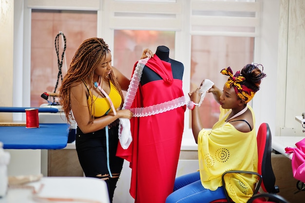 Duas costureiras africanas projetaram um novo vestido vermelho em manequim no alfaiate Meninas costureiras negras