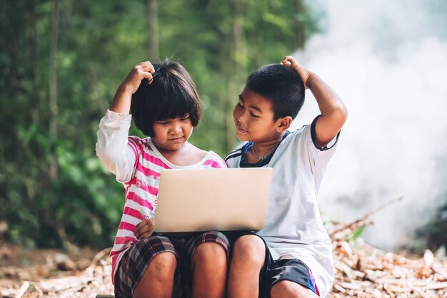 Duas crianças asiáticas se perguntando quando estudam via laptop em casa elearning escola remota no upcountry