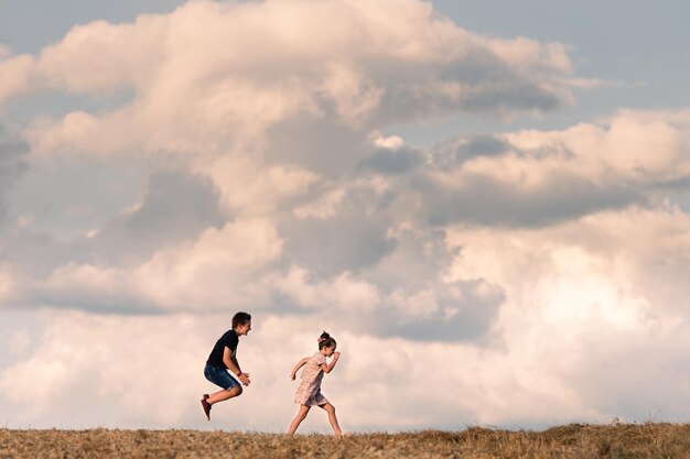 Duas crianças brincando e pulando no horizonte ao pôr do sol com um céu dramático e nuvens