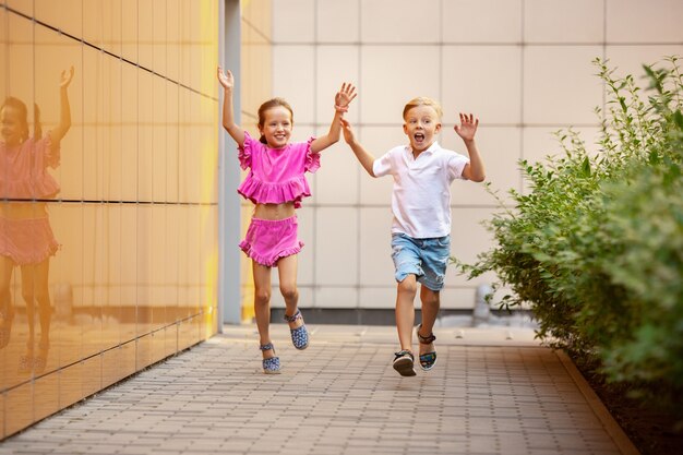 Duas crianças sorridentes, menino e menina correndo juntos na cidade, cidade em dia ensolarado.