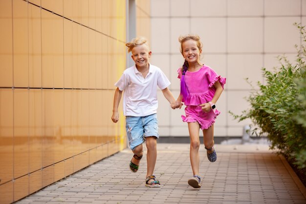 Duas crianças sorridentes, menino e menina, correndo juntos na cidade no dia de verão