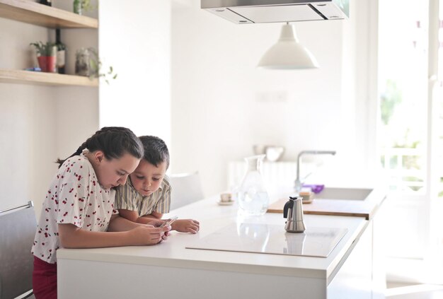 Duas crianças usam um smartphone na cozinha