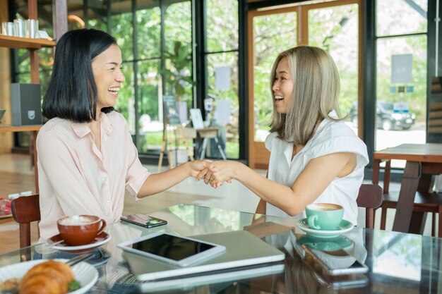 Duas empresárias apertando as mãos no café local. Duas mulheres discutindo projetos de negócios em um café enquanto tomava um café. Conceito de inicialização, ideias e tempestade cerebral. usando laptop no café.