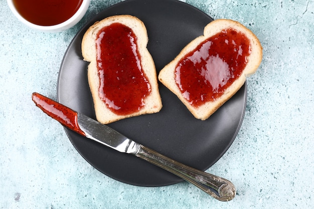 Duas fatias de pão com geléia de morango em uma placa preta.