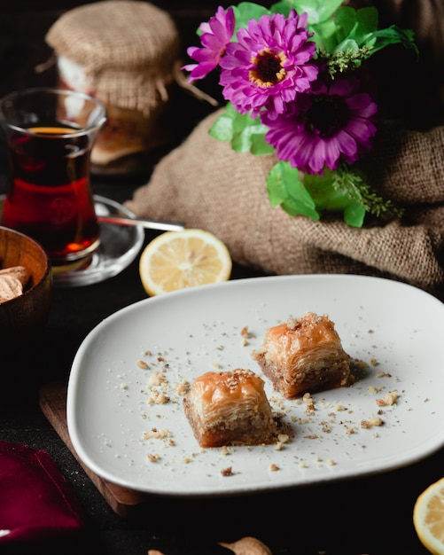 Duas fatias de sobremesa turca pakhlava com um copo de chá e limão fatia.