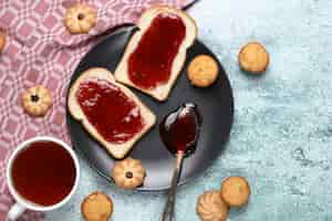 Foto grátis duas fatias de torrada com geléia vermelha em chapa preta com biscoitos ao redor