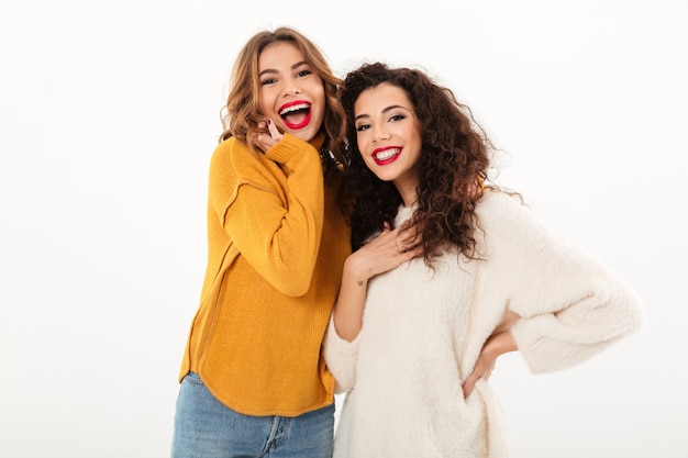 Duas garotas alegres em blusas posando juntos sobre parede branca