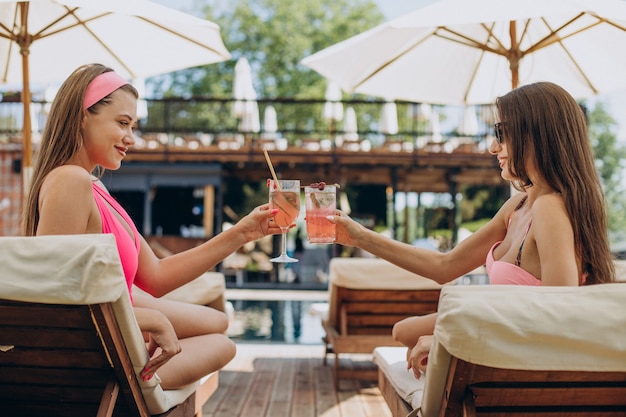 Duas garotas atraentes tomando coquetéis à beira da piscina