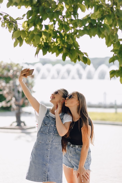 Duas garotas bonitas passeando no parque tirando fotos de si mesmas ao telefone