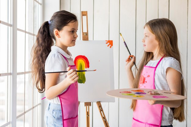 Duas garotas bonitas pintando na tela olhando uns aos outros