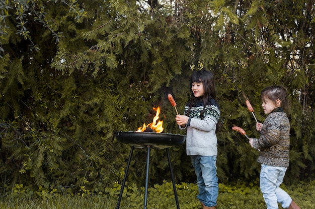 Duas garotas com salsichas em pé perto de churrasco