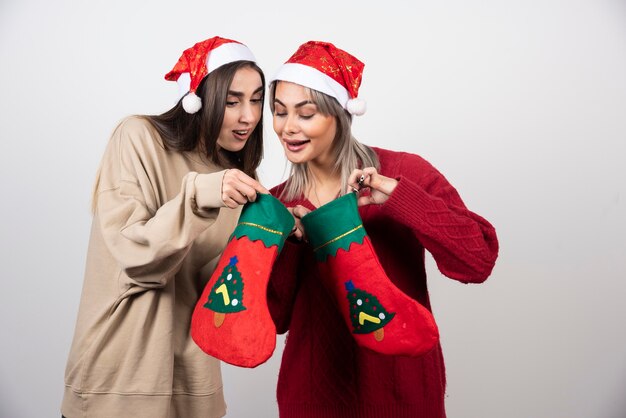 Duas garotas sorridentes com chapéu de Papai Noel, olhando as meias de Natal.