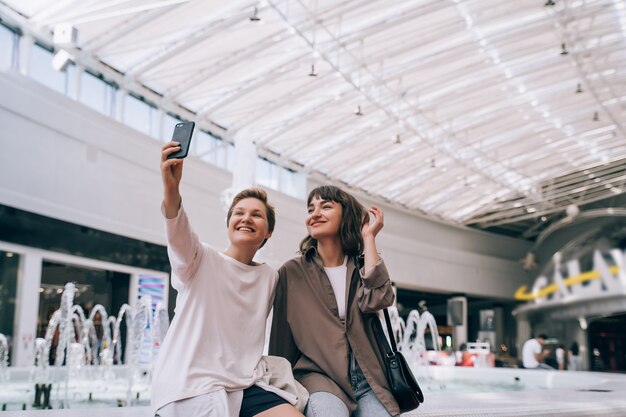 Duas garotas tiram uma selfie no shopping, uma fonte